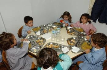 Un grupo de niños, en el comedor de un centro con su menú escolar.