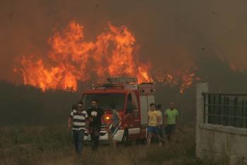 Un fuego virulento asoma tras el camión de extinción y de varios vecinos, que huyen de las llamas, en A Merca. A la derecha, el cierre de una casa. (Foto: MARCOS ATRIO)