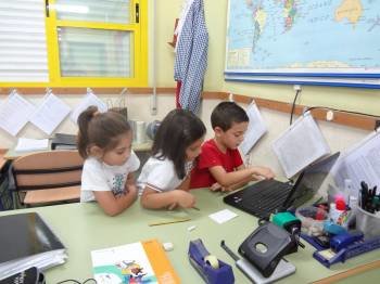 Tres niños pequeños realizan un trabajo con un ordenador en un aula.