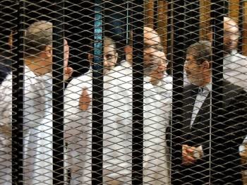 Mursi, con traje, charla con otros acusados tras las rejas.