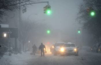 Peatones y vehículos se abren paso a duras penas por una calle nevada, en Nueva York. (Foto: JUSTIN LANE)