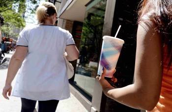Dos mujeres con sobrepeso caminan por la calle, una de ellas con un enorme refresco.