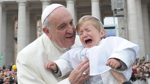 El papa Francisco saluda a un bebé vestido de papa a su llegada a la plaza de San Pedro en el Vaticano 