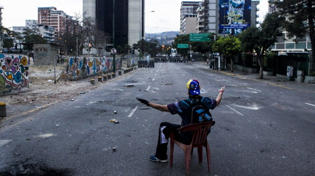  Un manifestante se sienta en una calle frente a los miembros de la Guardia Nacional Bolivariana