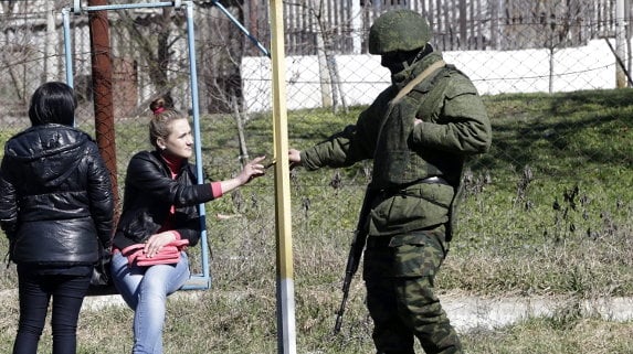 Un soldado armado sin identificar, presuntamente ruso, entrega un teléfono móvil a una joven