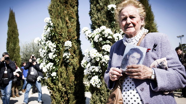 Una mujer sostiene una foto de una de las víctimas durante el homenaje, en el Bosque del Recuerdo del parque del Retiro