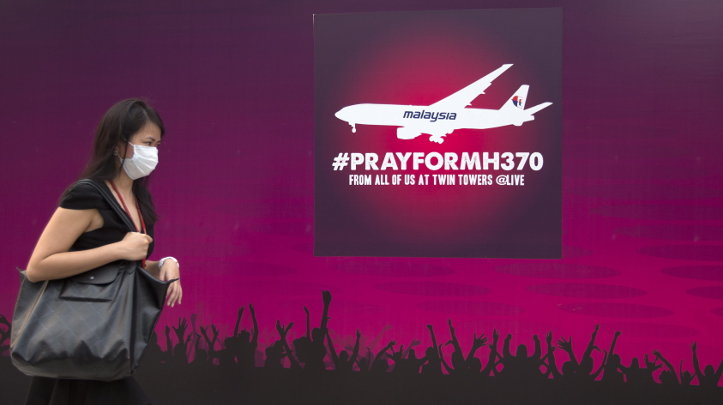 Una mujer camina frente a un aviso que dice &#39;#PrayforMH370&#39; por el vuelo desaparecido de Malaysia Airlines 