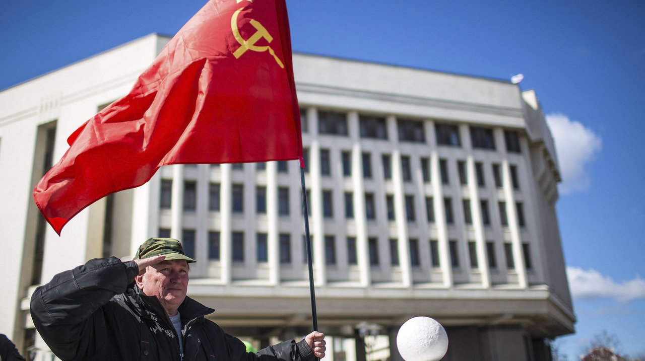 Un hombre sostiene una bandera soviética mientras realiza un saludo militar delante del Parlamento