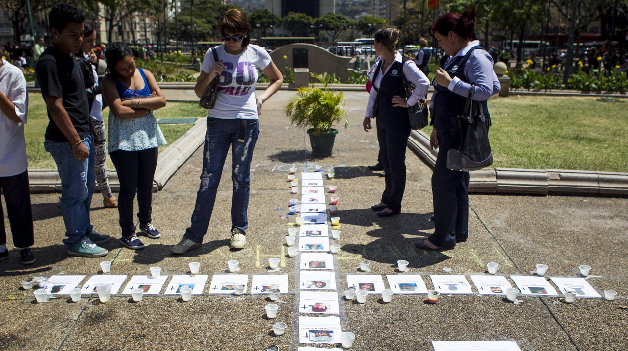 Varias personas observan una cruz hecha con fotos de los fallecidos en las protestas en Venezuela (MIGUEL GUTIÉRREZ)