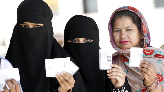 Mujeres muestran sus documentos de identidad mientras esperan su turno para ejercer su derecho al voto en Nueva Delhi
