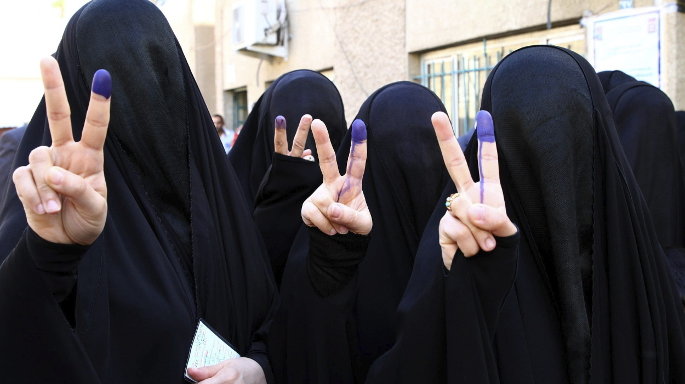 Mujeres muestran, mediante el símbolo de la victoria, su dedo índice marcado tras haber ejercido su derecho al voto en un colegio electoral en Bagdad