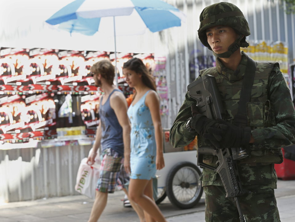  Un par de turistas extranjeros pasan junto a un soldado que vigila una calle de Bangkok
