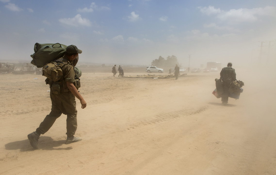 Soldados israelíes cargan con su equipo mientras se dirigen a tomar un transporte militar mientras se levanta un campamento cerca de la franja de Gaza