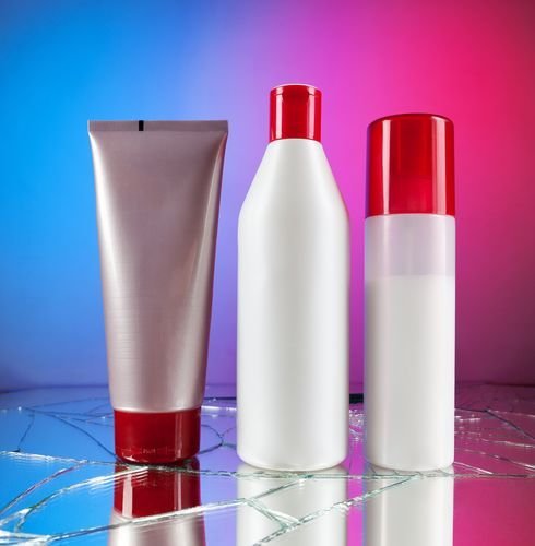 Group of empty cosmetic bottles with red caps on beautiful blue red mirror