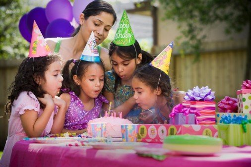 Hispanic girl blowing out candles at outdoor birthday party