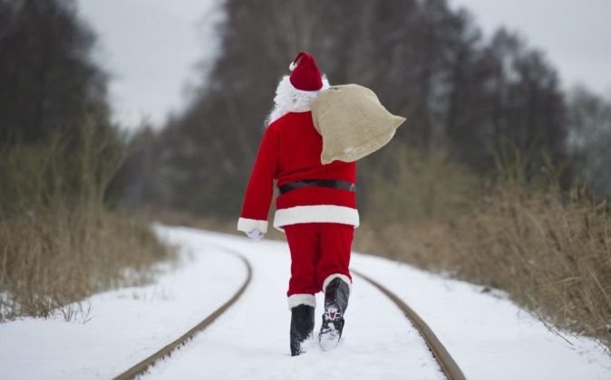 Un Santa Claus camina por una vía del tren cubierta de nieve.