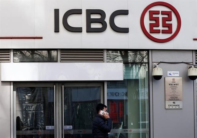 Un viandante utiliza su iPhone mientras pasa delante de una sucursal del banco Industrial and Commercial Bank of China.