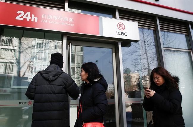 Una viandante utiliza su iPhone (dcha) mientras pasa delante de una sucursal del banco Industrial and Commercial Bank of China.