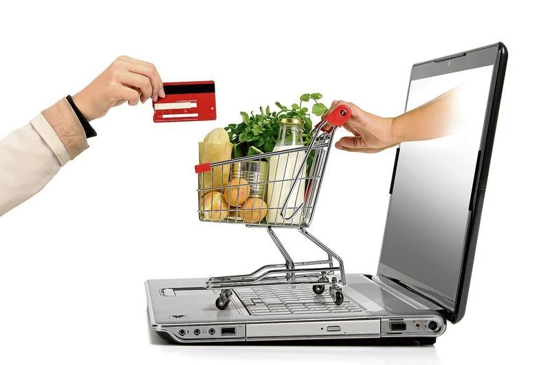 Hand with credit card and a small shopping cart coming from  laptop screen isolated in white