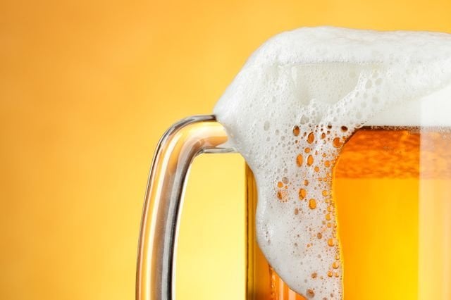 Beer mug with froth over yellow background