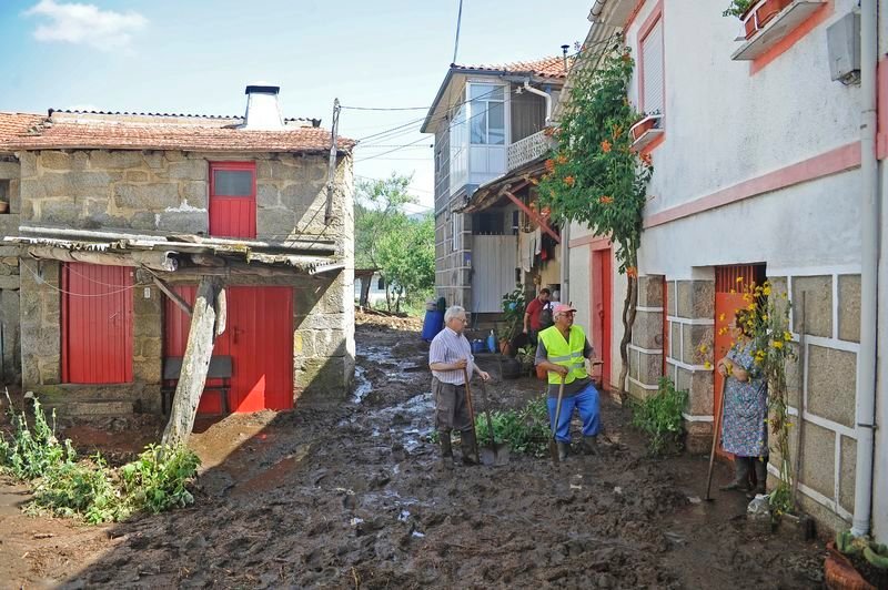 Tres vecinos conversan este martes, el día después de la riada, mientras limpian el lodo en una calle en el centro de la localidad de Infesta (MARTIÑO PINAL).