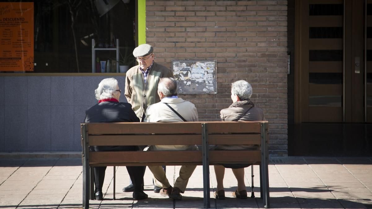 Un grupo de personas mayores conversa a media tarde en un banco de la calle.