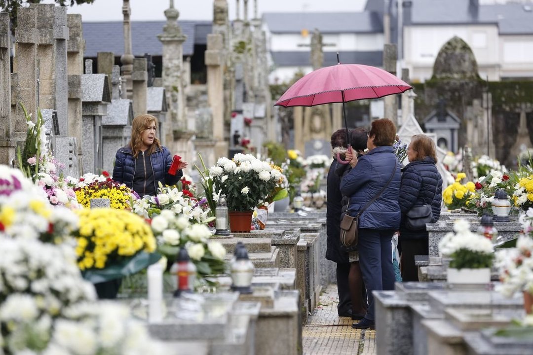 Un grupo de mujeres se protege de la lluvia entre un mar de flores en el cementerio de Verín, durante la mañana de este viernes.
