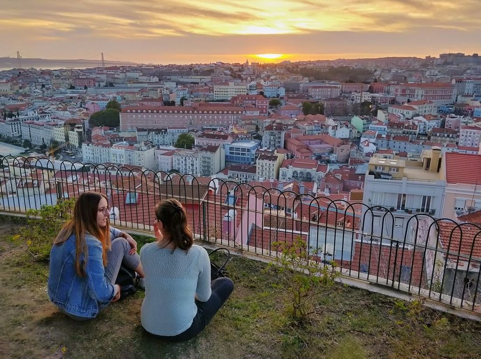 Dos chicas conversan delante de una vista panorámica de Lisboa. (Foto: Unsplash)