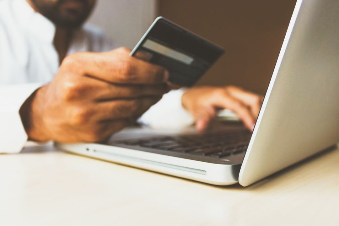 Un hombre utiliza el ordenador mientras mira su tarjeta de crédito. (Foto: Unsplash) compra online