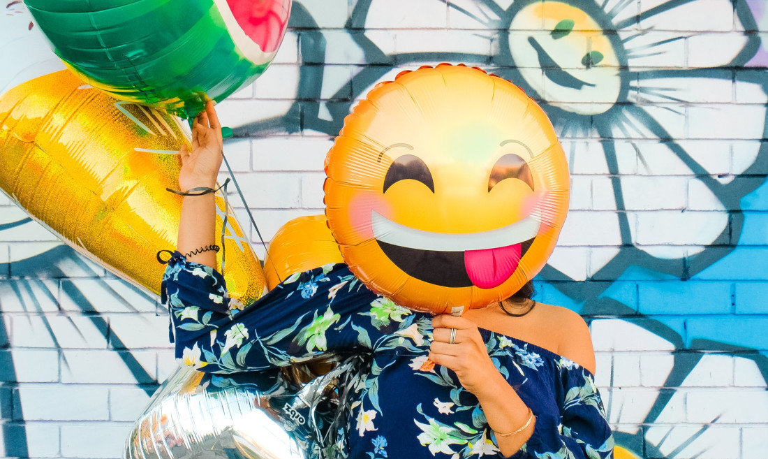 Una mujer se tapa la cara con un globo en forma de emoji. (Foto: Unsplash)