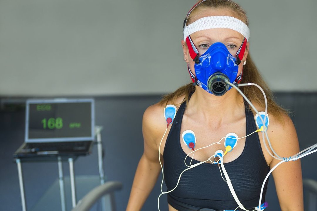 Female athlete having a VO2 test with a VO2 mask on her face, electrocardiogram pads attached, pulse rate 168 BPM, treadmill