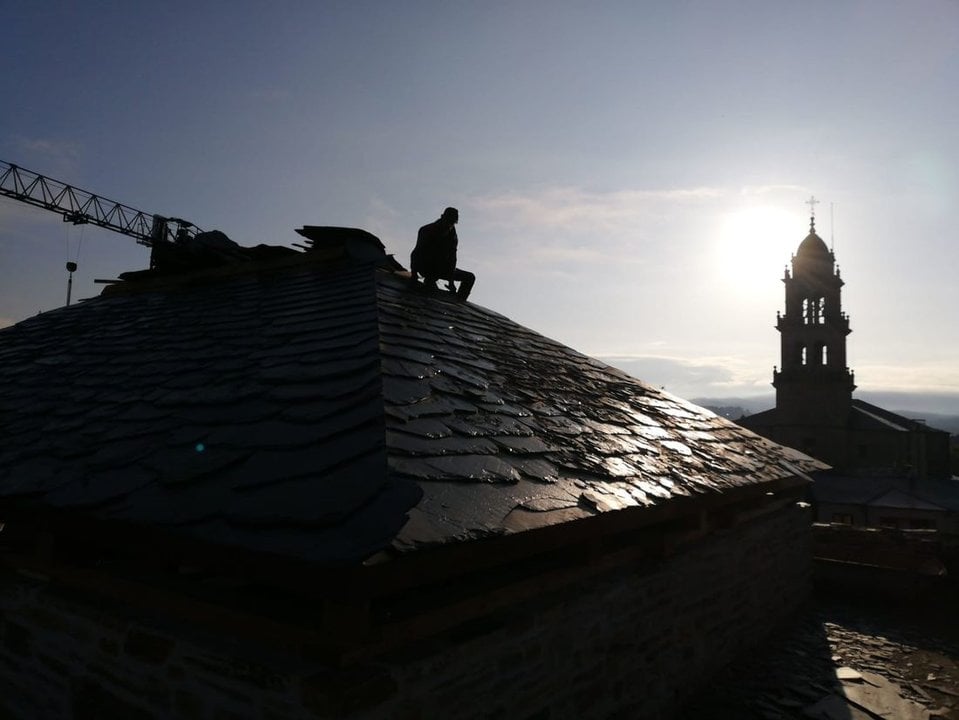 Un operario coloca pizarra en un tejado en una localidad gallega.