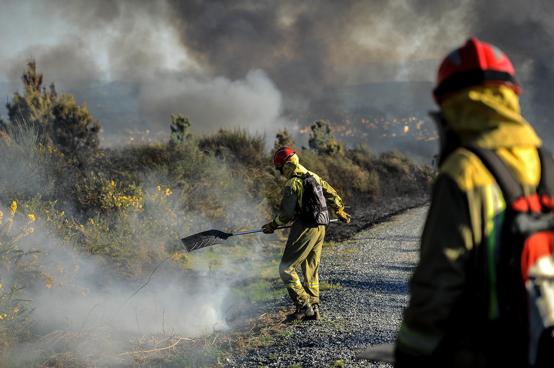 Dos brigadistas apagan un fuego que se declaró hace un año en un monte de Carballiño.