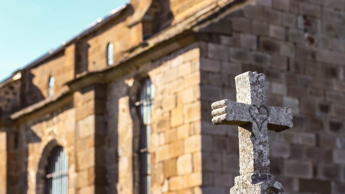 Una cruz de piedra junto a una iglesia. (Foto: Unsplash)