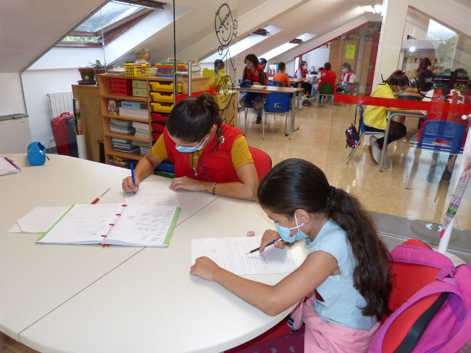 Voluntarios de Cruz Roja ayudan a los niños usuarios con las tareas escolares.