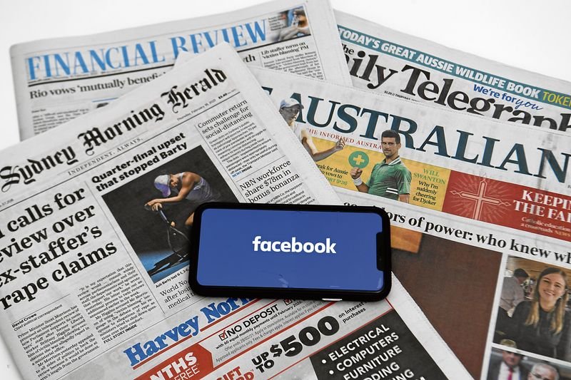 Un teléfono móvil con el fondo de pantalla de Facebook reposa sobre varios periódicos australianos.
