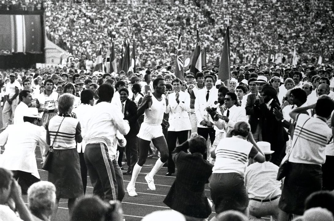 Rafer Johnson porta la antorcha entre una multitud en el estadio olímpico de Los Ángeles.