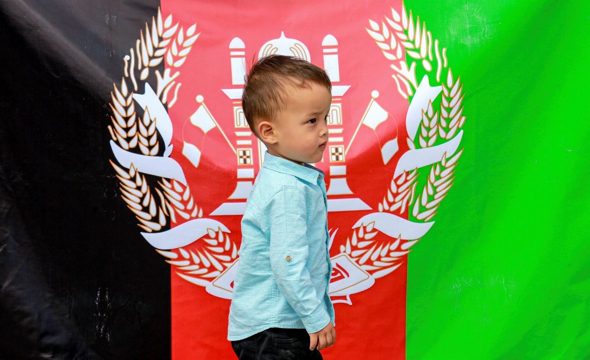 Un niño pasa caminando ante la bandera oficial de Afganistán