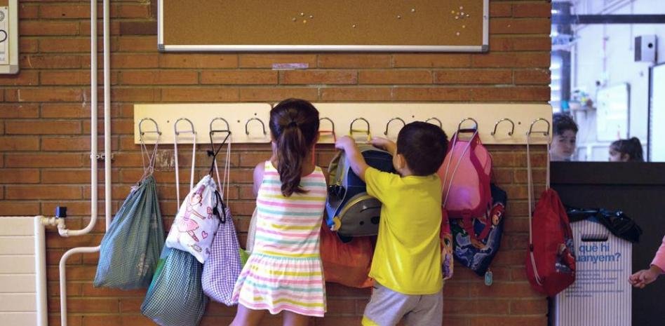 Dos niños colocan sus mochilas en los percheros de su clase de primaria.