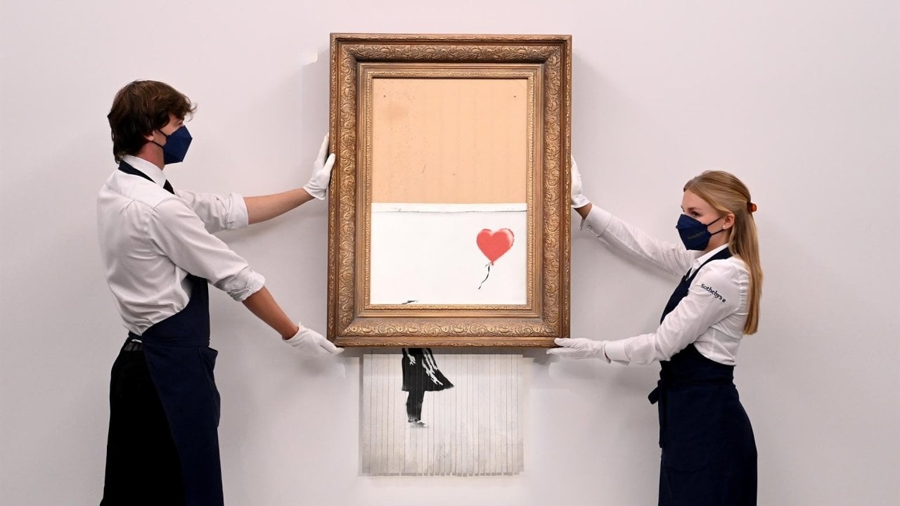 Dos empleados de Sotheby's sostienen el cuadro 'Love is in the bin' de Banksy. EFE/EPA/FACUNDO ARRIZABALAGA