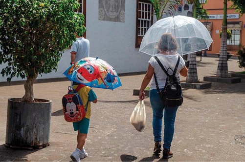 <p> Un niño, acompañado por su madre y protegido con un paraguas, se dirige al colegio en La Palma. </p>