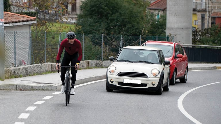 Un ciclista circulando al lado del arcén con dos coches tras él (MARTIÑO PINAL).