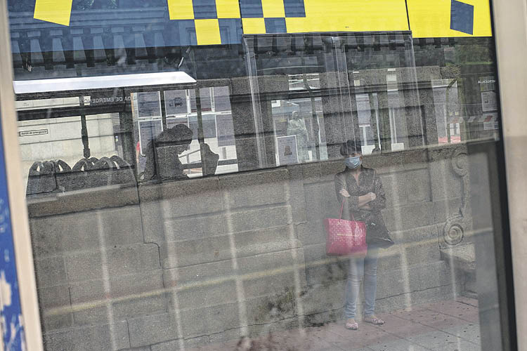 Una viajera, en la parada del autobús urbano mirando uno de los autocares.