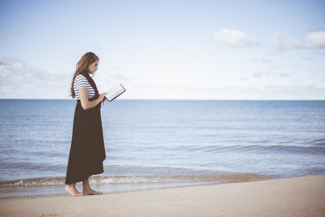 Mujer con ibro en la playa. Imagen de Pexels en Pixabay.
