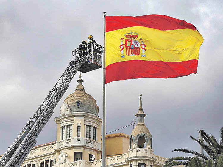Dos bomberos reparan una bandera española en Alicante.