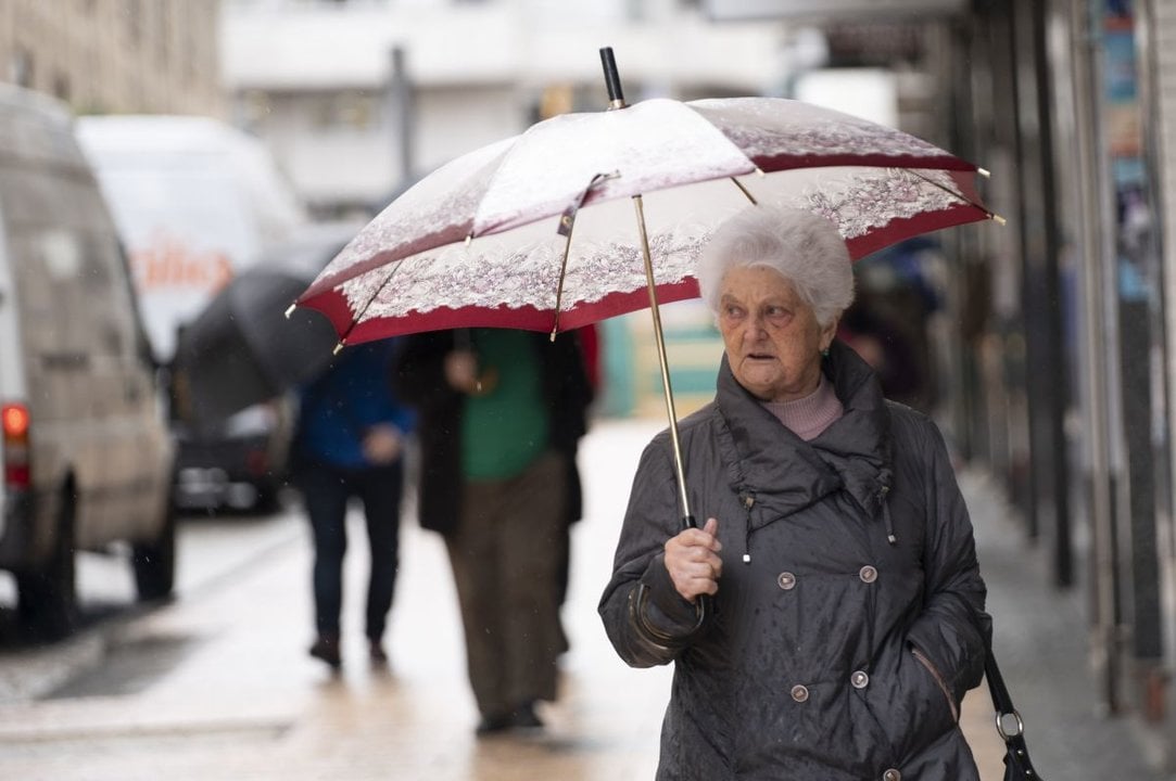 Una pensionista pasea bajo la lluvia en una de las calles de la ciudad.
