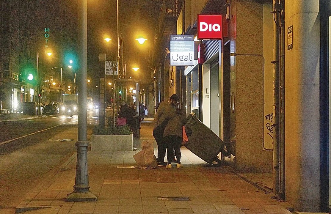 Un hombre y dos mujeres buscan alimentos en un contenedor situado junto a un supermercado de la ciudad. MARTIÑO PINAL
