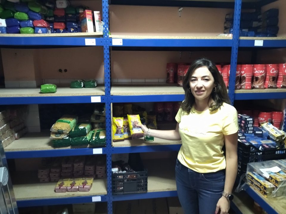 La trabajadora social, Isabel Álvarez. ante las estanterías con grandes vacíos.