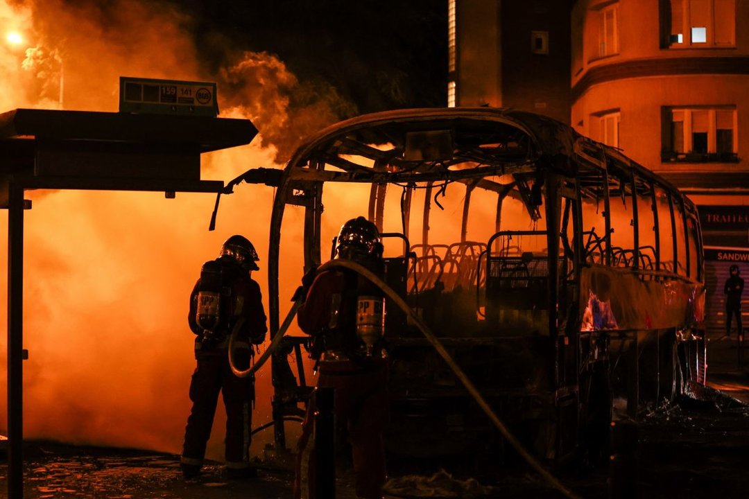 Los bomberos apagan un autobús quemado durante los enfrentamientos entre manifestantes y la policía antidisturbios.