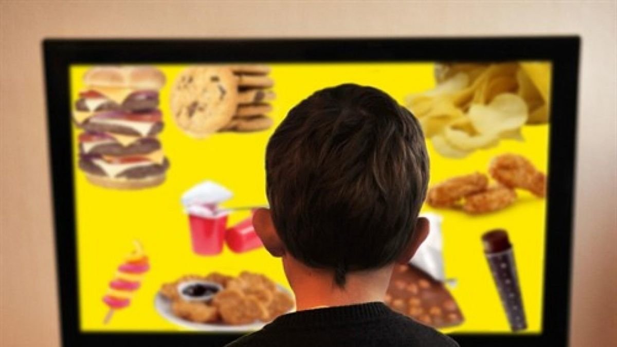 Un niño frente a una pantalla publicitaria de comida rápida.